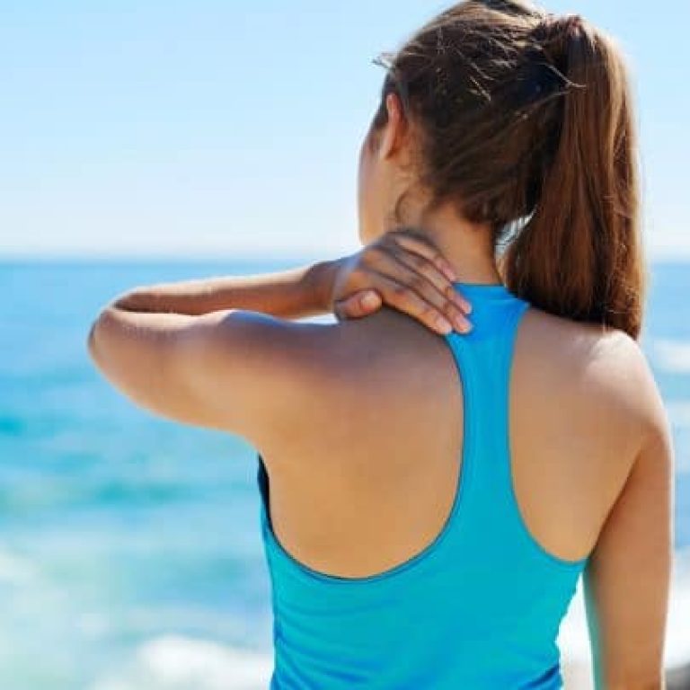 Femme de dos face à la mer avec une douleur d'épaule
